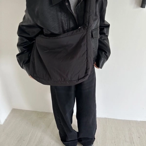 Black padded puffer tote bag with wide strap worn by model against minimalist background