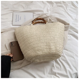 Detail of hand-woven straw tote with natural bamboo handles on a white fabric background