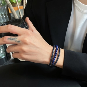 Men's blue onyx beaded bracelet and woven leather wristband set on a wrist holding a cup