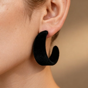 Close-up of vintage black flocked C-shaped earrings worn to show velvet texture and size