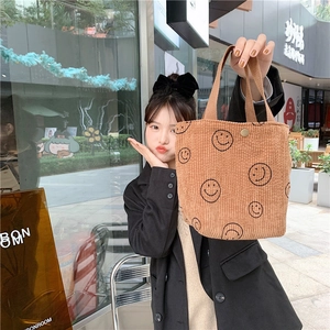 Close-up of brown corduroy tote bag with black smiley face embroidery and metal buckle