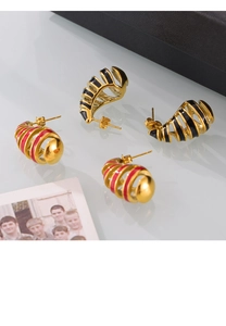 Detail of spiral enamel stud earrings in gold, black and red finish on a mirror surface