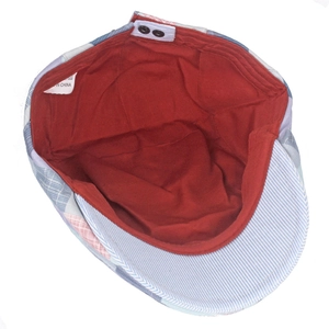 Detail of colorful plaid beret featuring red lining, metal buckles, and fabric care label