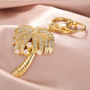 Détail du porte-clés palmier doré avec cristaux et perles sur fond en soie rose