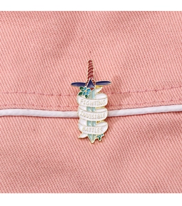 Macro detail of sword enamel pin with Fighting Invisible Battles text on denim fabric