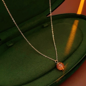 Macro shot of orange crystal pendant on gold plated necklace in green velvet jewelry box