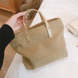 Detailed texture of woven light camel tote bag with creamy leather handles and gold rivets