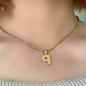 Dettaglio ravvicinato della collana in acciaio dorato con ciondolo lettera P e maglia Figaro