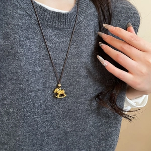 Golden rocking horse necklace pendant with brown cord shown on a grey knit sweater