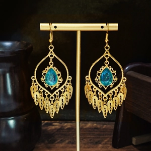 Golden ethnic drop earrings with blue gemstones and leaf tassels on a T-bar stand