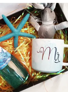 Gift box detail with marble ceramic mug, teal starfish, plush rabbit, and orange raffia