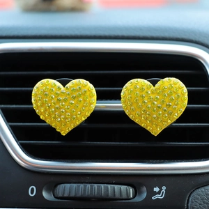 Close-up of sparkling yellow rhinestone heart car air vent clips on a dark interior grill