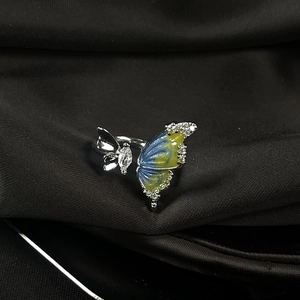 Close-up of enamel butterfly ring with blue-yellow gradient and zircons on dark silk