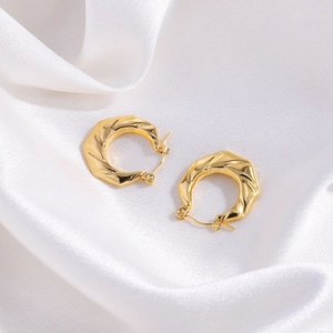 Close-up of golden asymmetric floral earrings with irregular hammered texture on white silk