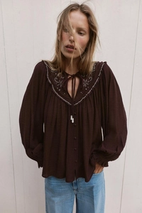 Detailed view of white ethnic embroidery and tassel ties on a bohemian textured shirt
