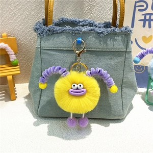 Cute yellow plush monster keychain with purple horns hanging on a blue denim bag