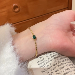 Détail d'un bracelet torsadé plaqué or 18k avec une pierre verte taillée en émeraude