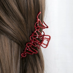 Detail view of a bright red claw clip with white ink spots on long brown hair
