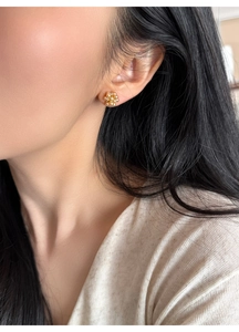 Detailed close-up of a gold floral stud earring with cluster pearls and crystal center