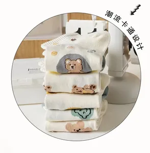 Close-up of five pairs of white cotton socks featuring cute brown bear and green patterns