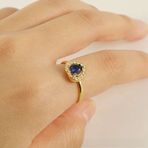 Detailed view of an adjustable gold heart ring featuring a blue gemstone and pavé diamonds