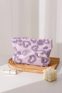 Detail of purple leopard plush makeup bag on wooden tray with cozy lifestyle props