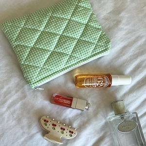 Close-up of green gingham quilted cosmetic bag with cherry hair claw on soft white fabric