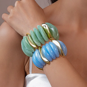 Detail shot of light blue and green acrylic bracelets with gold metal accents on wrist