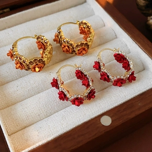 Detailed close-up of gold-plated rose hoop earrings with crystals in a wooden jewelry box