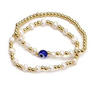 Detail of beaded bracelets featuring golden beads, freshwater pearls and blue evil eye