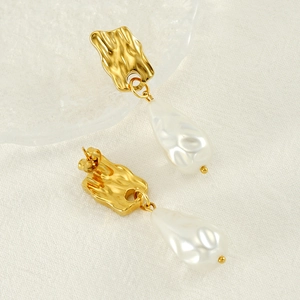 Elegant gold irregular metal studs with hanging baroque pearls on white fabric background