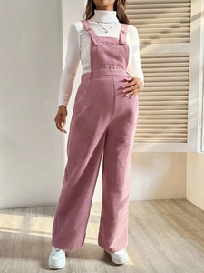 Pink corduroy maternity overalls styled with a white turtleneck and sneakers