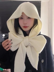 Detailed knit texture of a cream-white hooded scarf with a large decorative bow