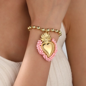 Detail eines Goldperlenarmbands mit einem Sacred Heart-Anhänger und rosa Akzenten