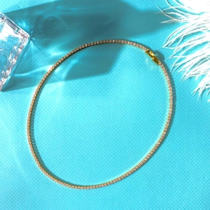 Elegant gold tennis necklace with white zircons on blue silk background for women
