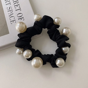 Détail macro du chouchou en satin noir orné de perles blanches élégantes sur fond blanc