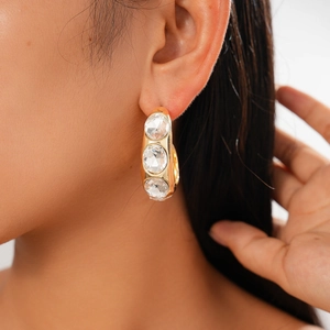 Close-up of gold C-shaped geometric earrings with three round diamonds on model