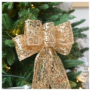 Detail of champagne gold sequined bow topper on a lit Christmas tree branch