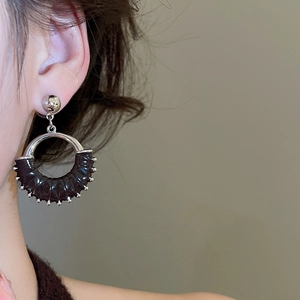 Close-up of vintage round earrings with silver metal frame and black pleated leather detail