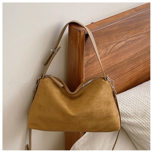 Detail of camel suede hobo bag with silver buckle hanging on a wooden bedframe