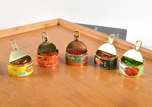 Detailed view of five miniature dollhouse food cans on a warm wooden tray surface