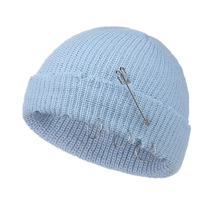 Close-up of light blue knit beanie featuring decorative silver metal rings and long safety pin
