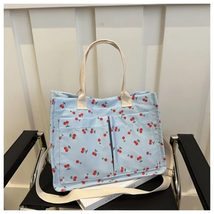 Detail of light blue canvas tote bag with red cherry print and beige webbed handles