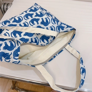 Detailed top view of a white canvas tote bag with blue cat patterns and zipper closure