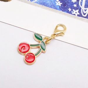 Close-up of cherry charm with red enamel, green leaves and gold lobster clasp for bags