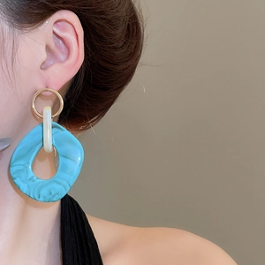 Close-up of model wearing irregular turquoise resin earrings with marble pattern and gold detail