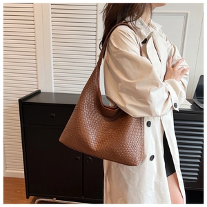 Detail of a large brown woven hobo tote bag showing textured craftsmanship on a model