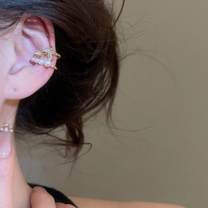 Gros plan d'un élégant ear cuff doré avec nœud en zircon et perles sur un modèle