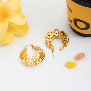 Détail de boucles d'oreilles en dentelle dorée avec motifs floraux sur fond blanc