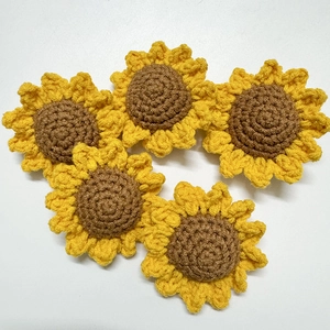 Flat lay of five handmade crochet sunflower yarn accessories on a white background